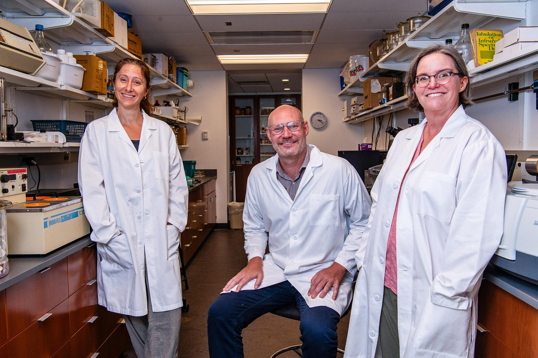 Three people standing in a science laboratory with white labcoats on.