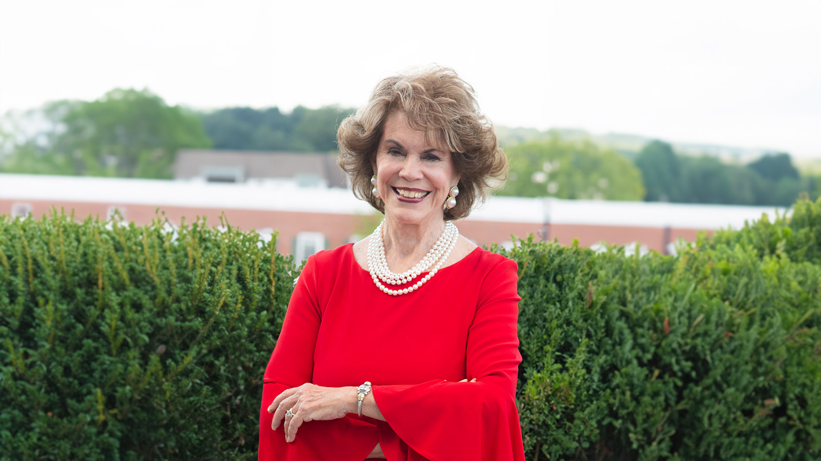 Person in a red dress and pearls smiling.