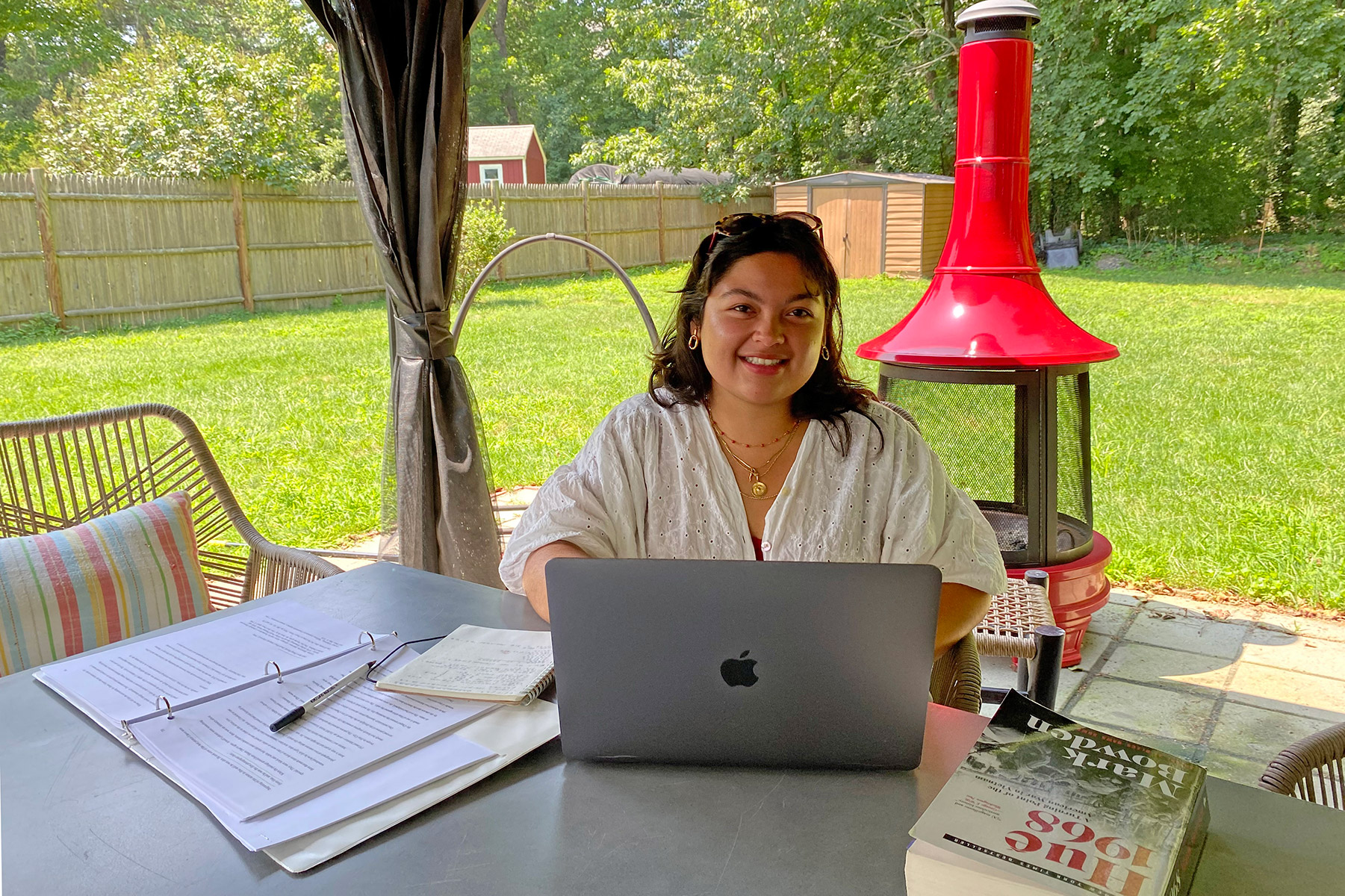 Person sitting outside at a table working on a computer with grass in the background.