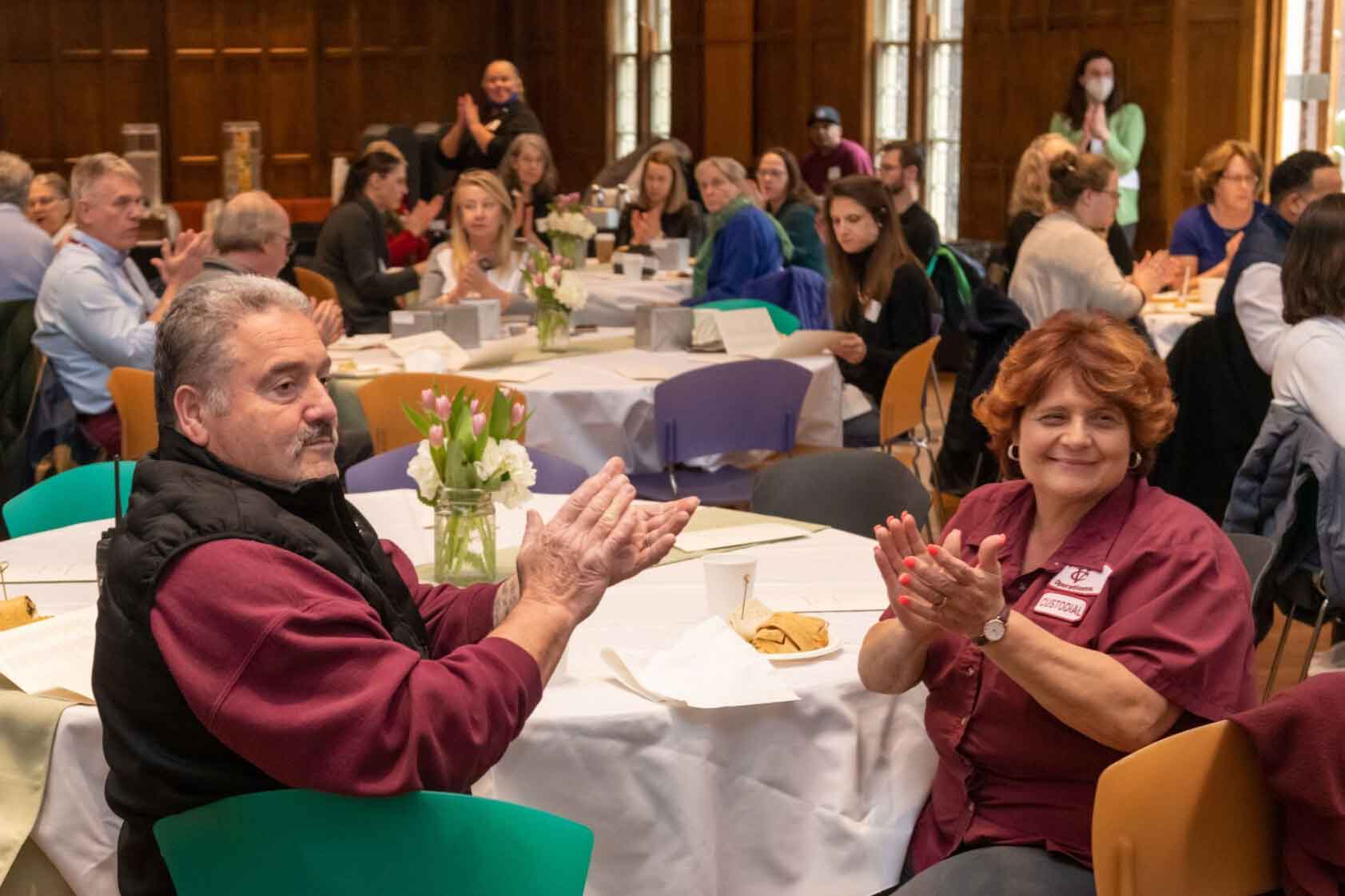 People seated at a table during a banquet clapping and smiling.