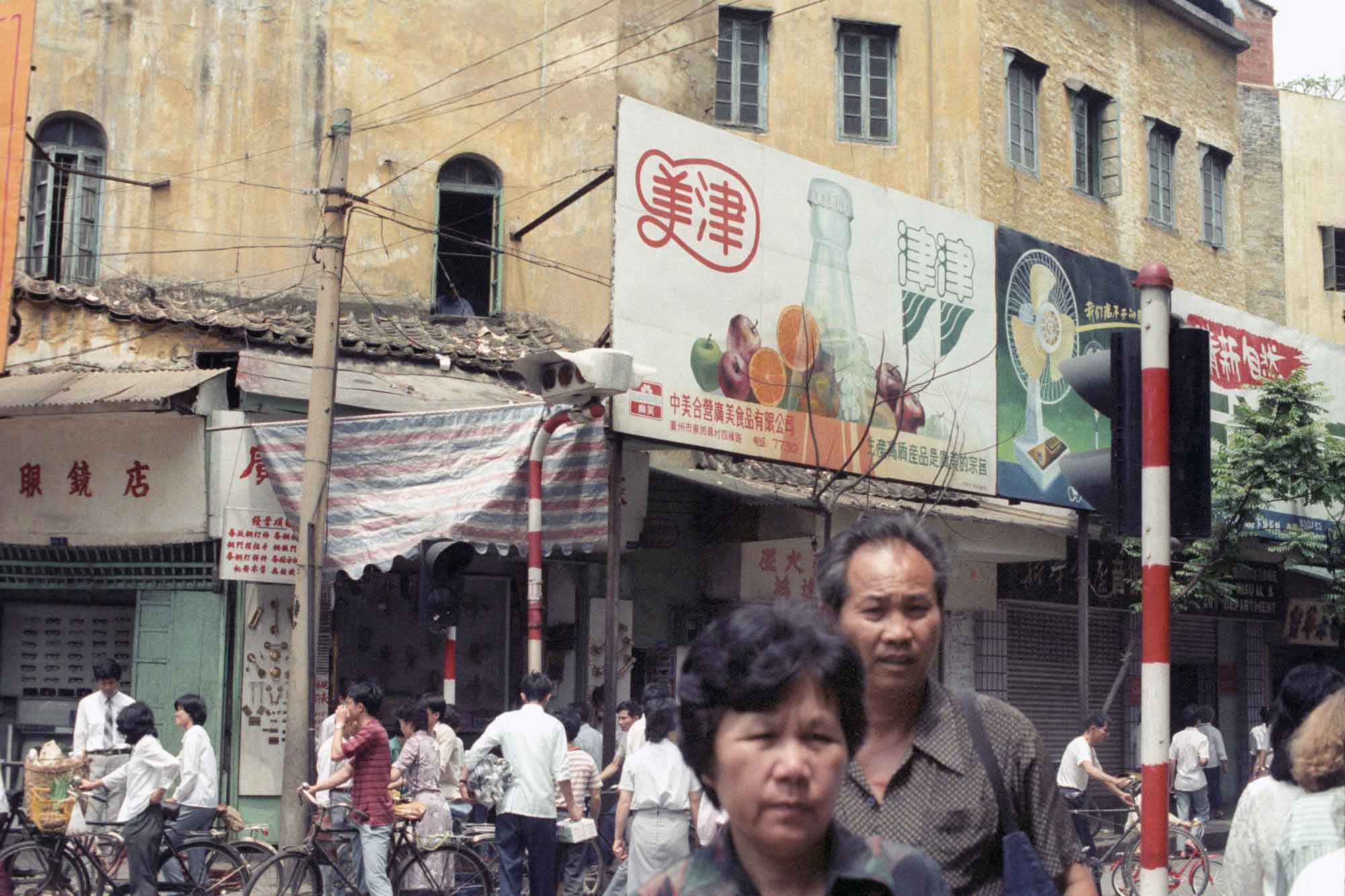 Busy street public corner with people walking around in the background and two people in the foreground walking towards the camera.