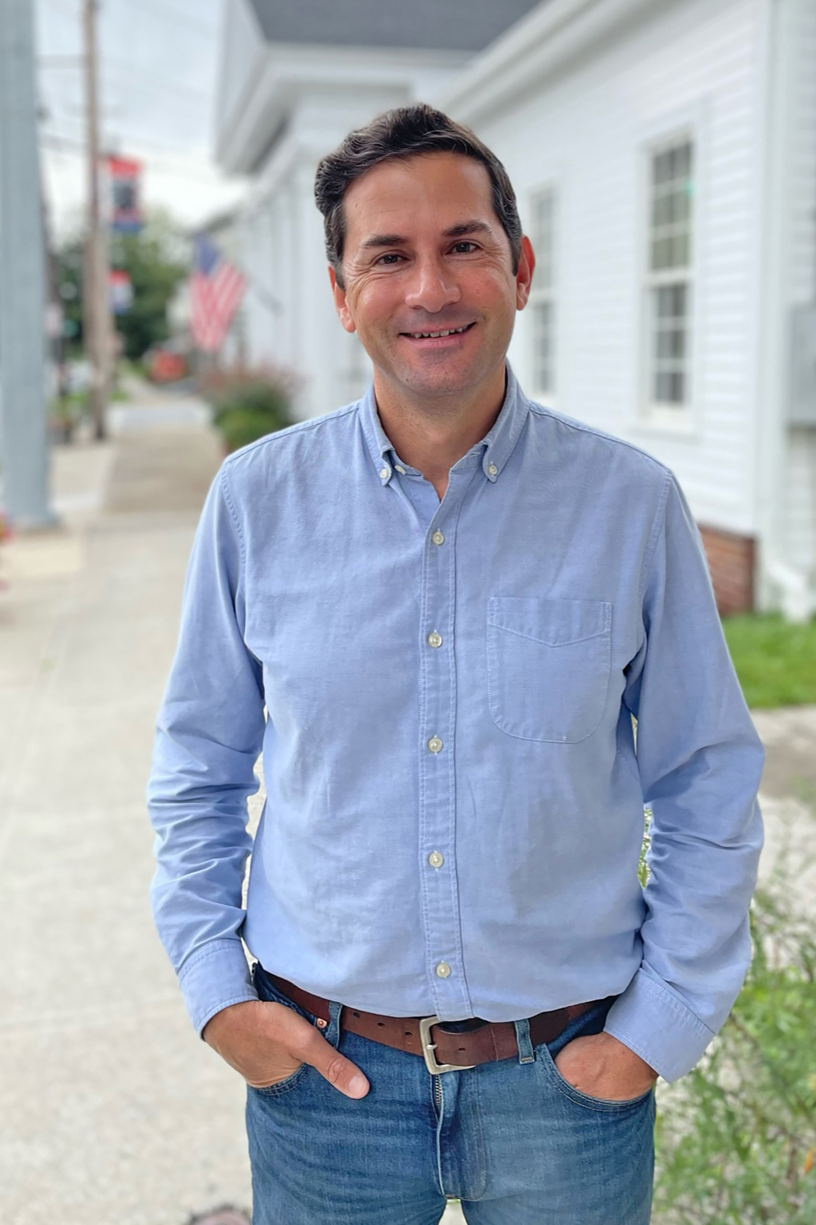 A person in a blue collared shirt and jeans facing the camera, smiling.