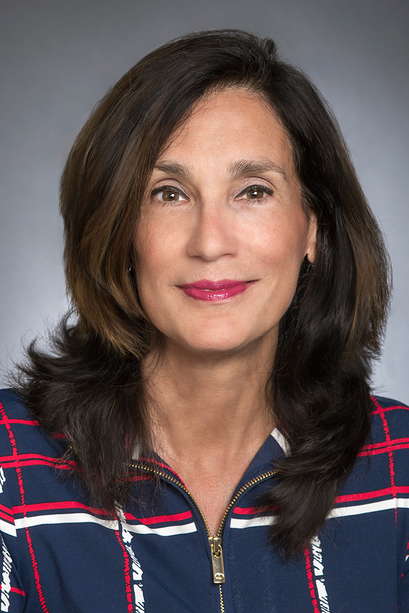 A studio portrait of a person with long brown hair facing the camera.