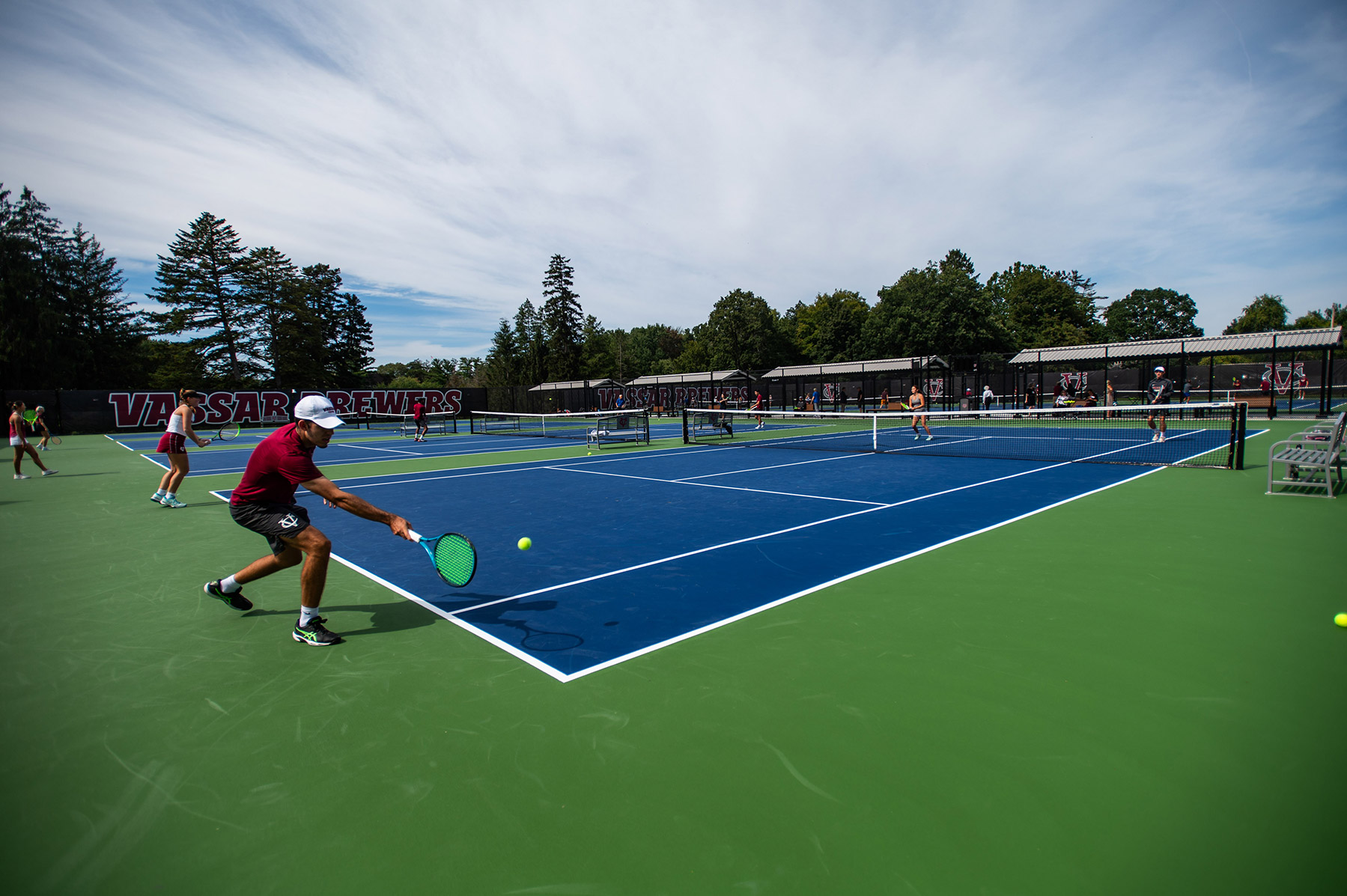 Photo of a tennis court from a corner with a person hitting a tennis ball in the foreground to a person across the net.