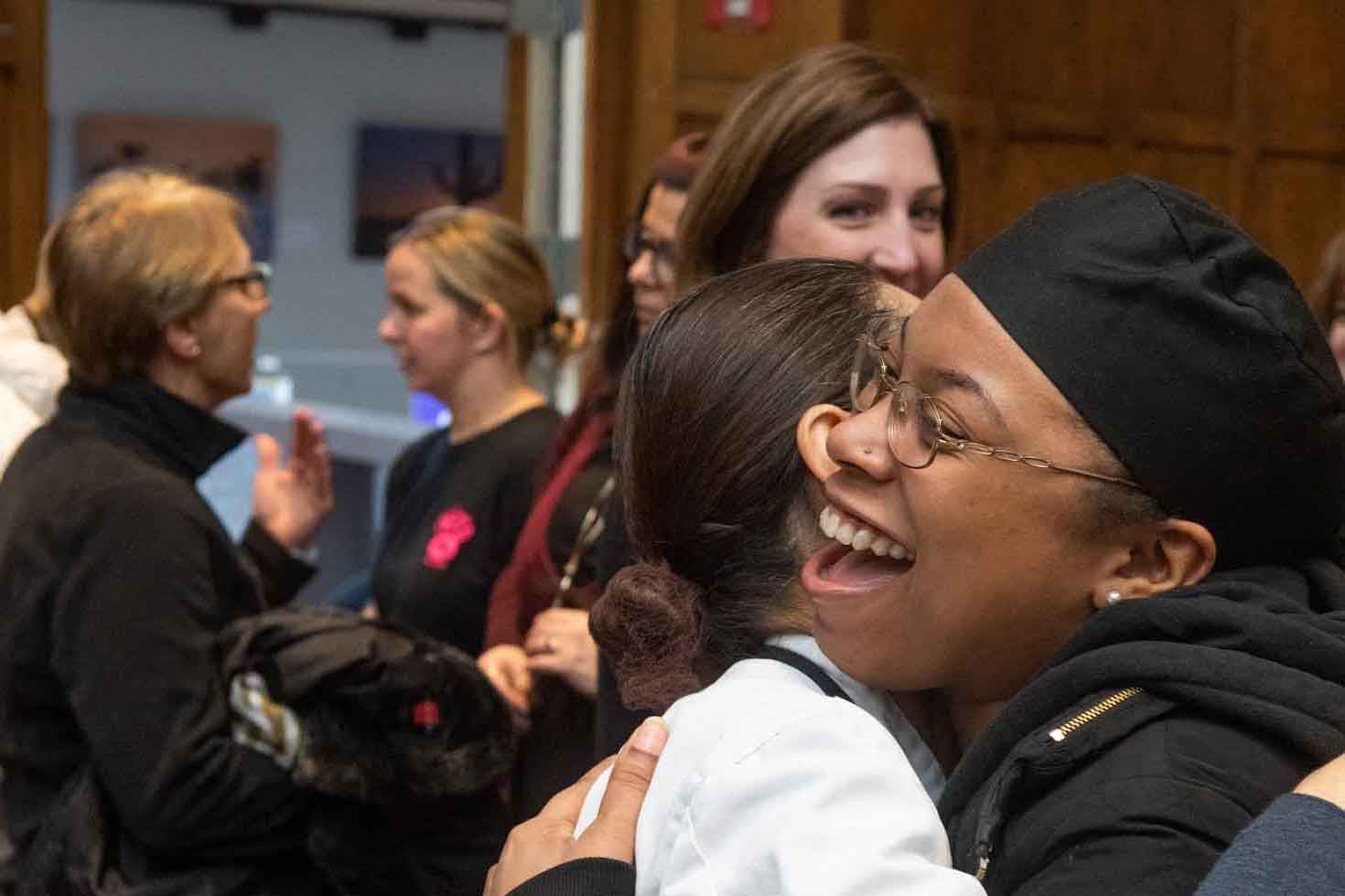 Two people in a front of a crowd smiling and hugging.