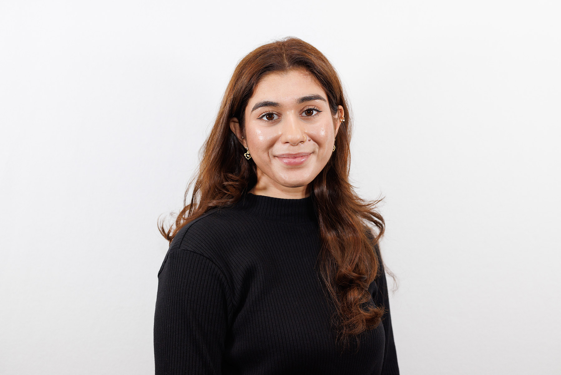 Person with long orange/brown hair with a black shirt posing in front of a white backdrop.