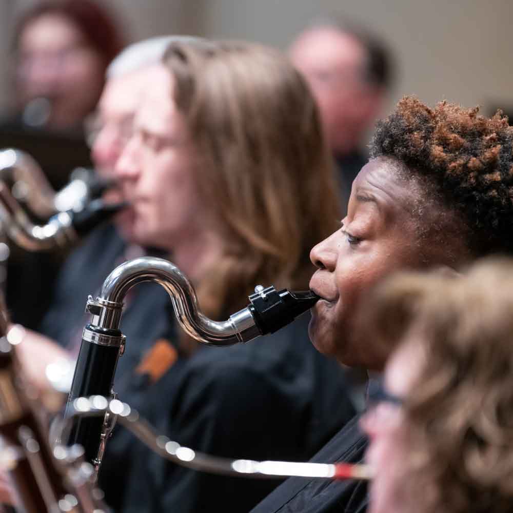 Sideview of people in an orchestra playing reed instruments.