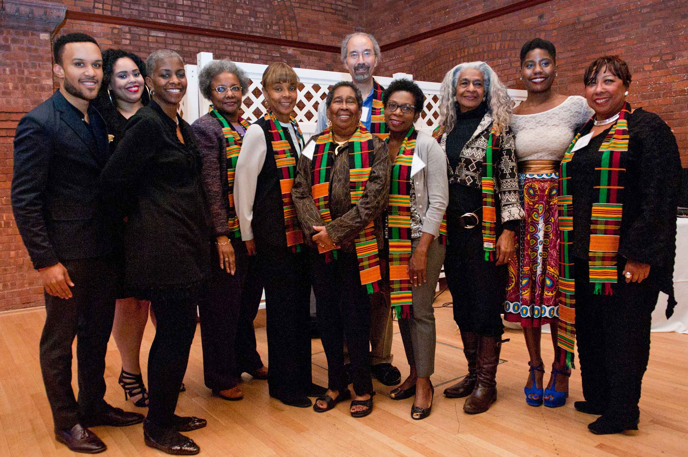 Group of people standing and smiling, some wearing kente cloths over their shoulder.
