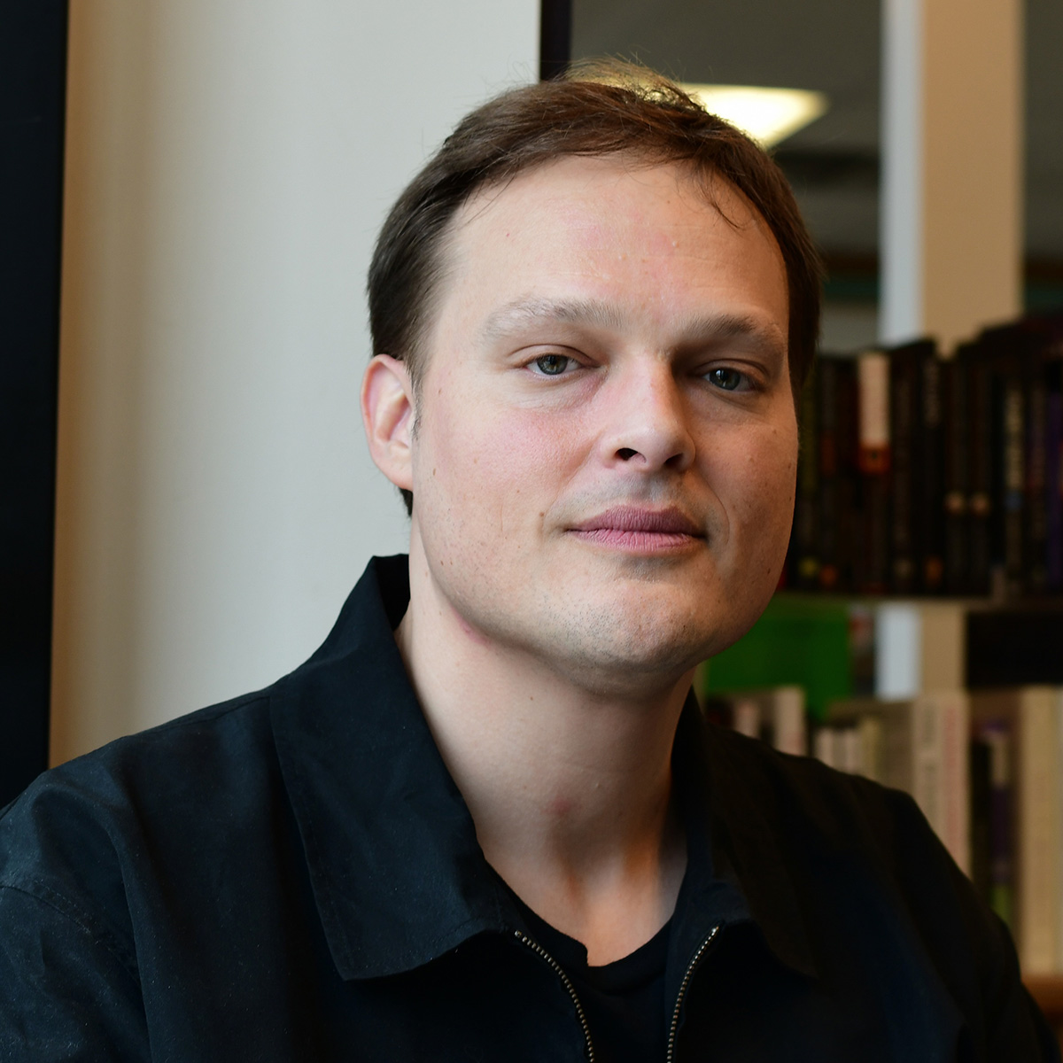 Garth Greenwell wearing a black collared shirt in front of a bookcase.