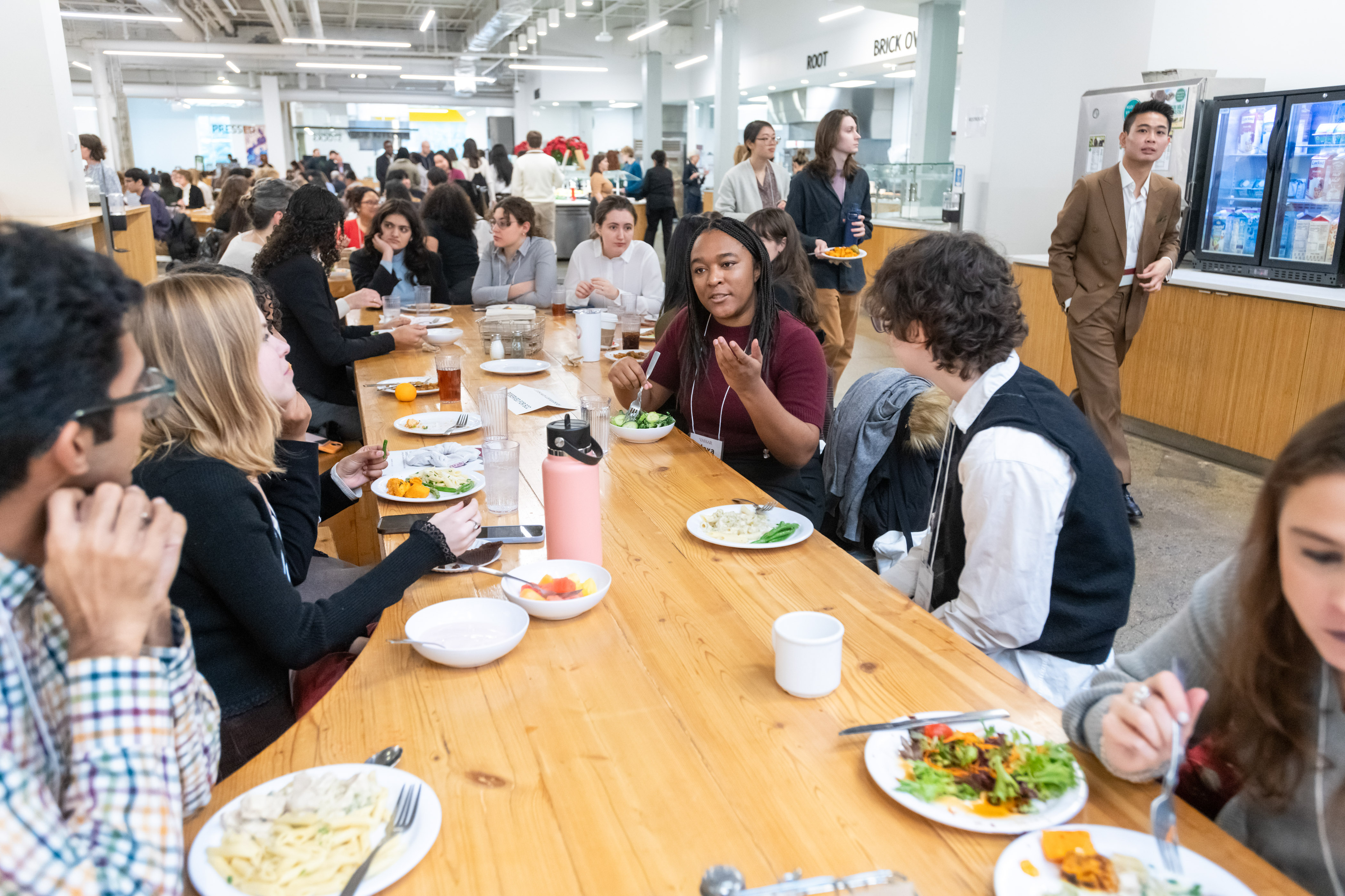 A long table with over eight people seated, listing to one person, while eating a meal.