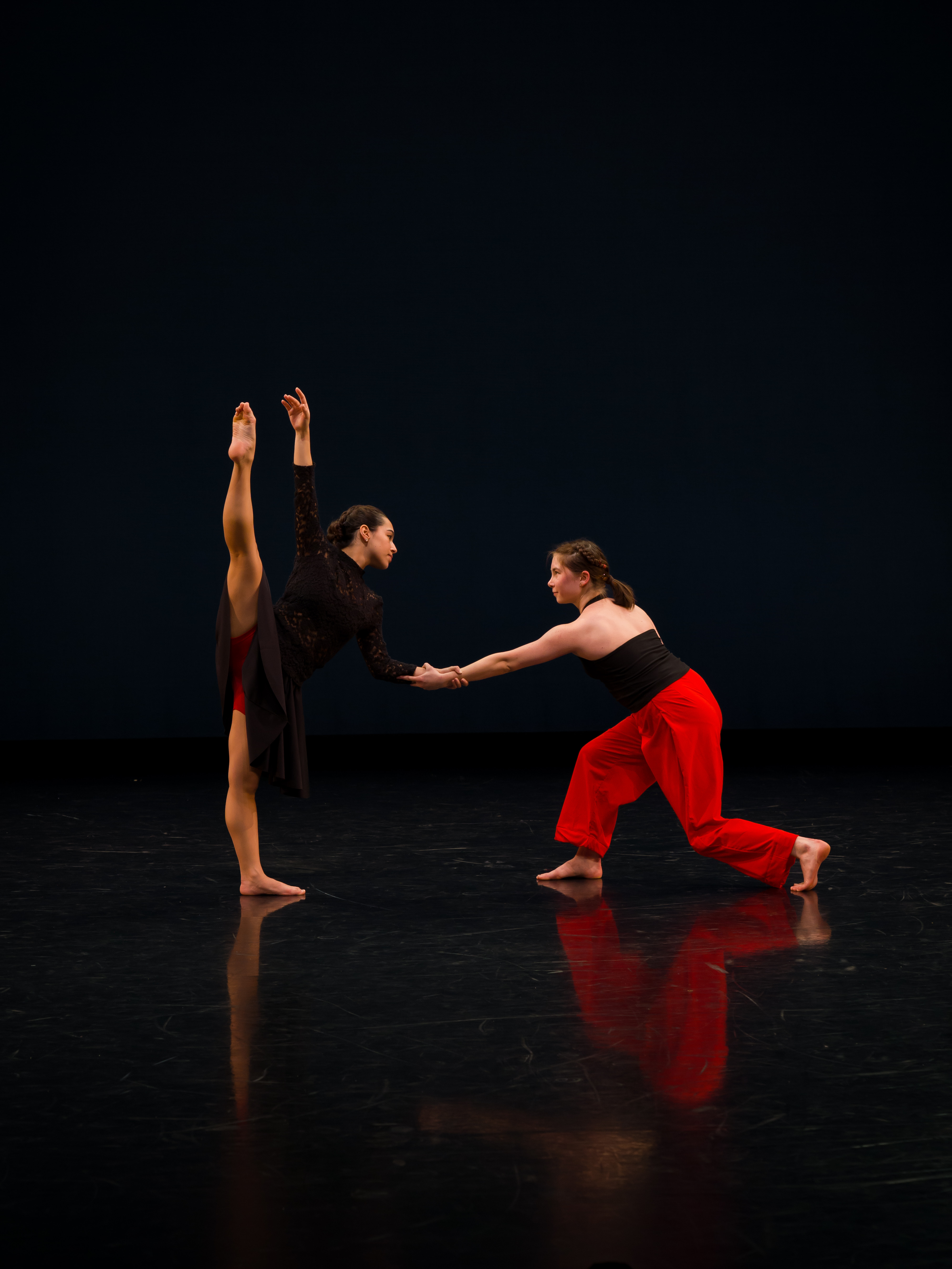 Two dancers hold hands while performing on a dark stage.