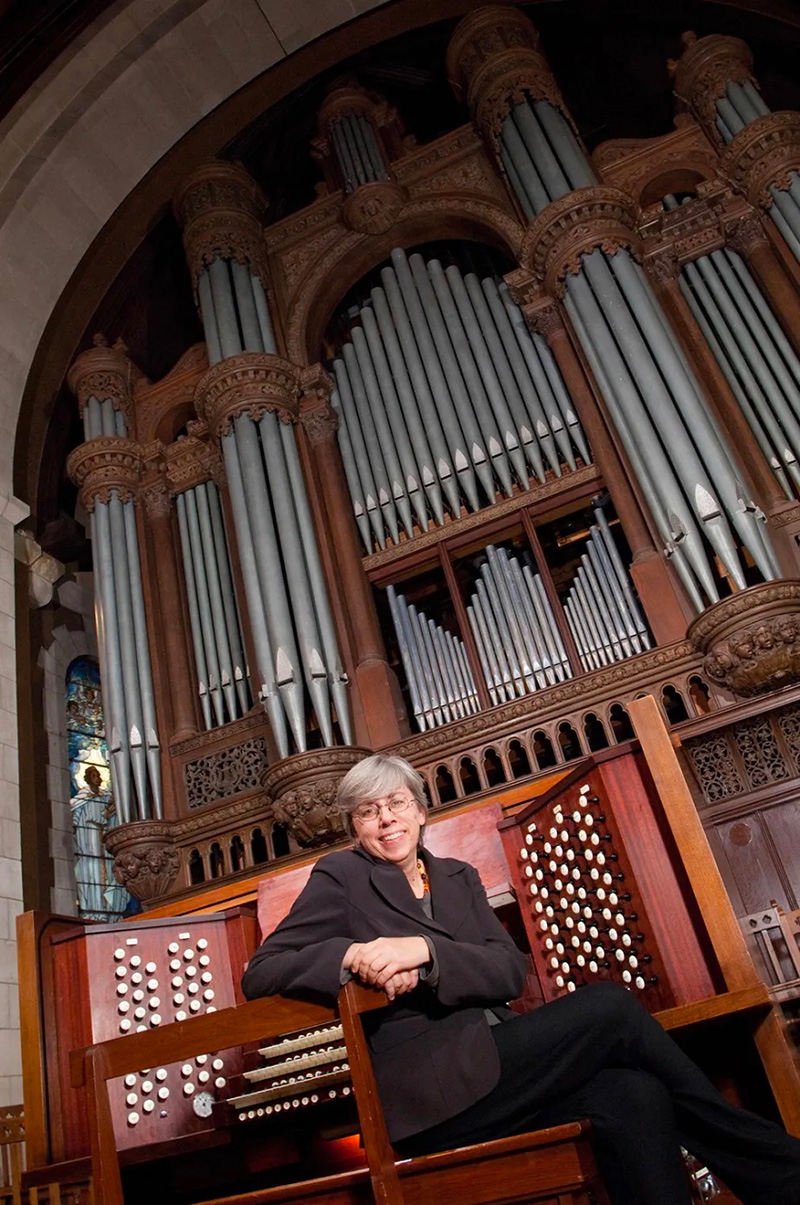 A person sitting in front of a floor-to-ceiling organ—a view of all the pipes.