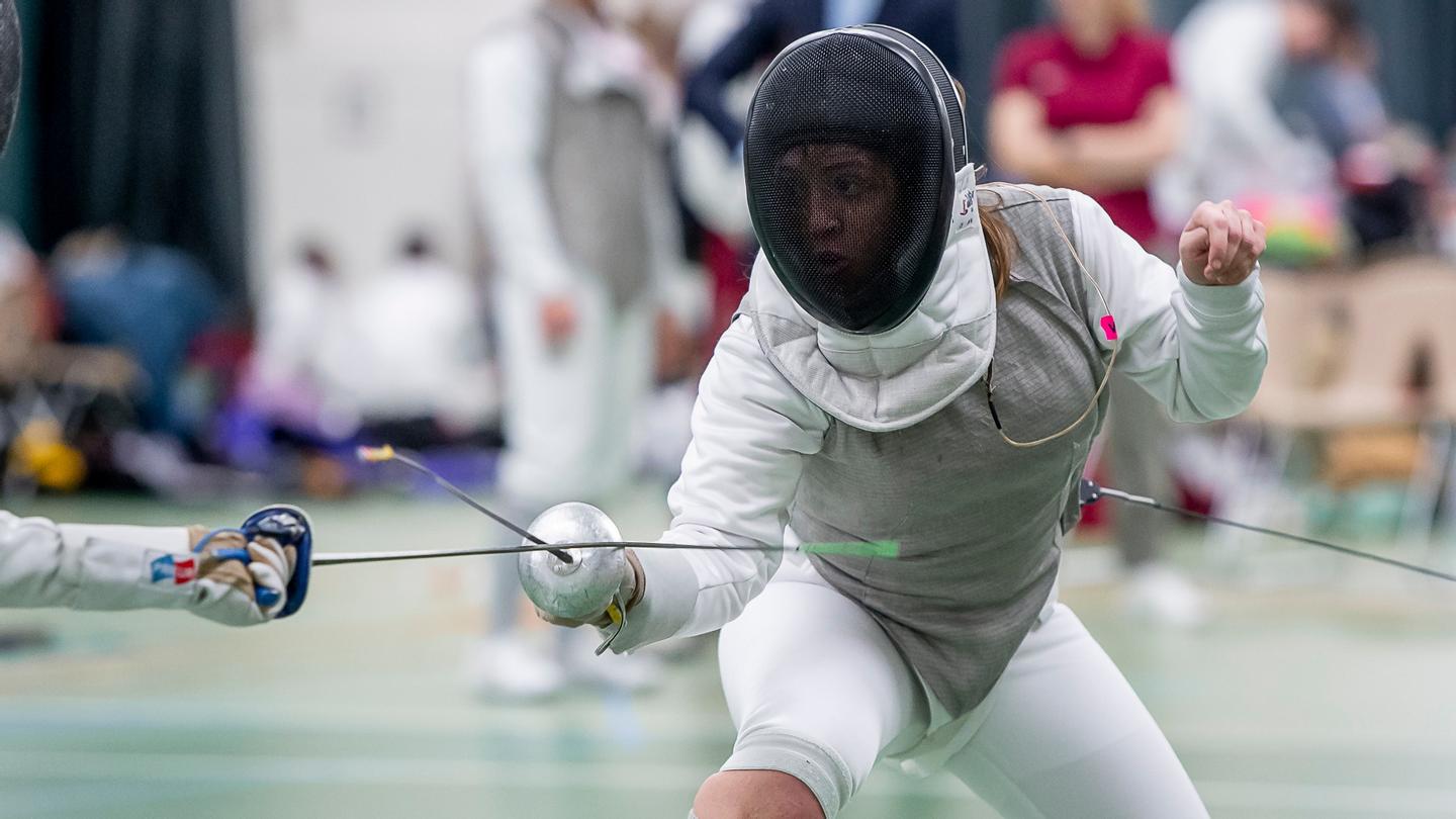 Person with fencing gear and a foil holding a defensive stance.