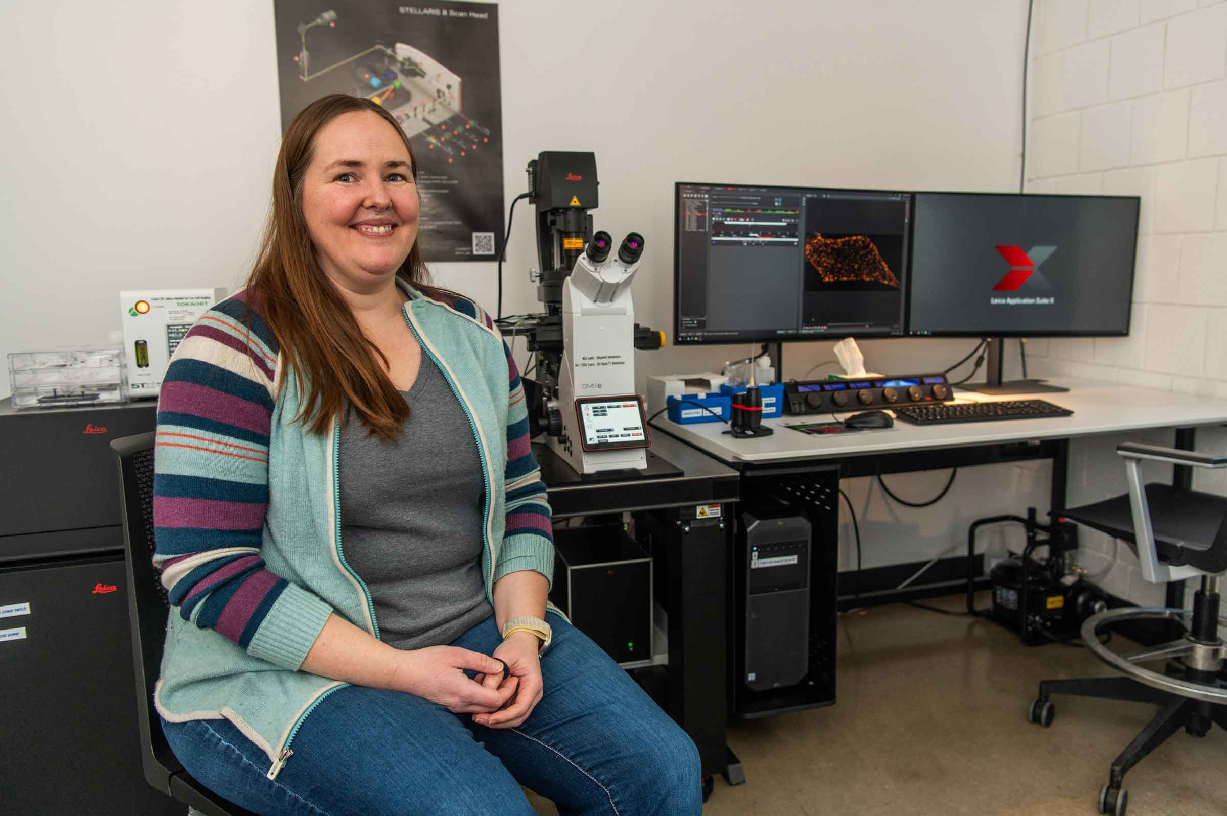 Person seated in front of a high tech microscope with a computer screen.