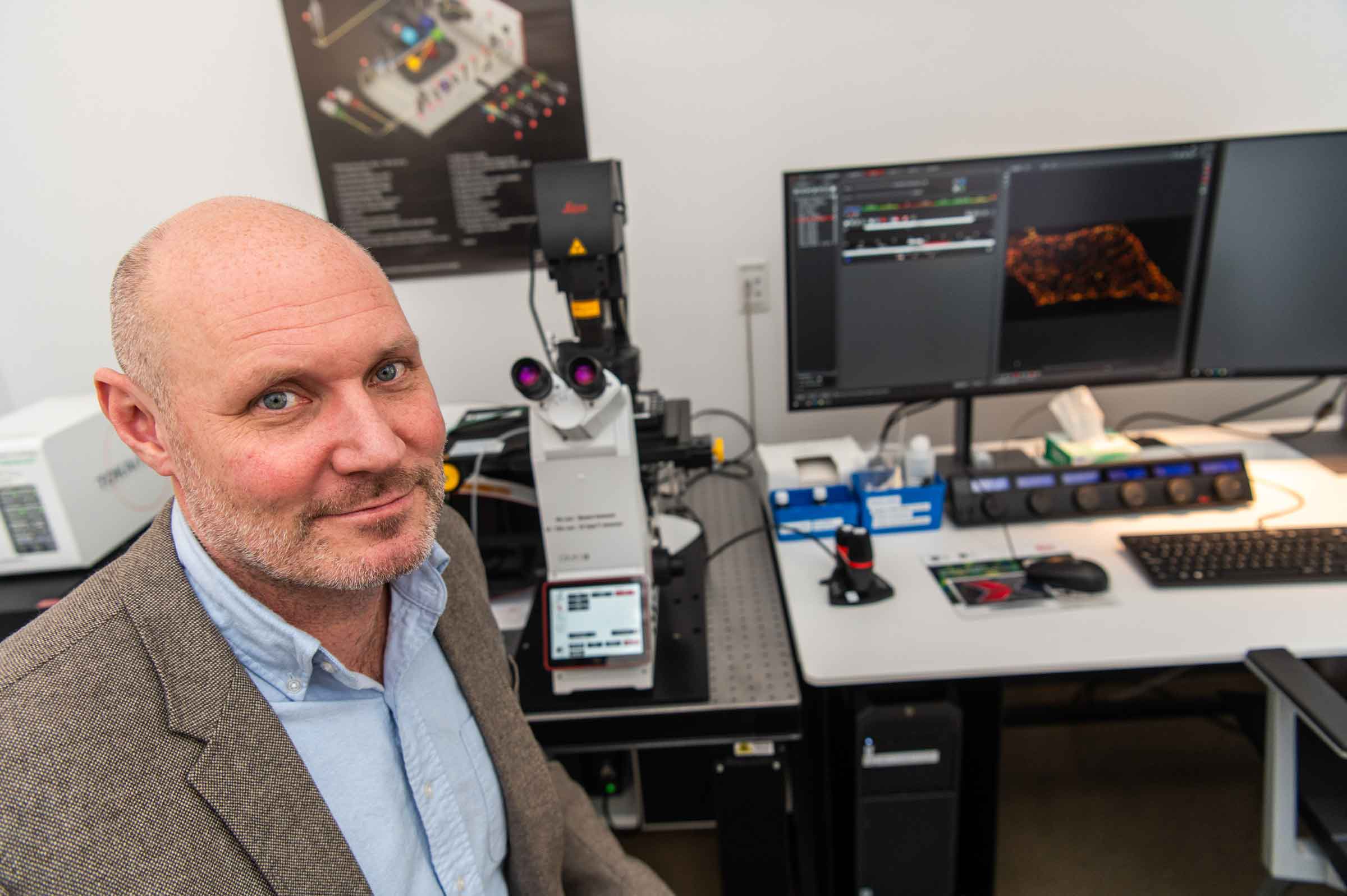 Person standing in front of a high tech microscope with a computer screen.
