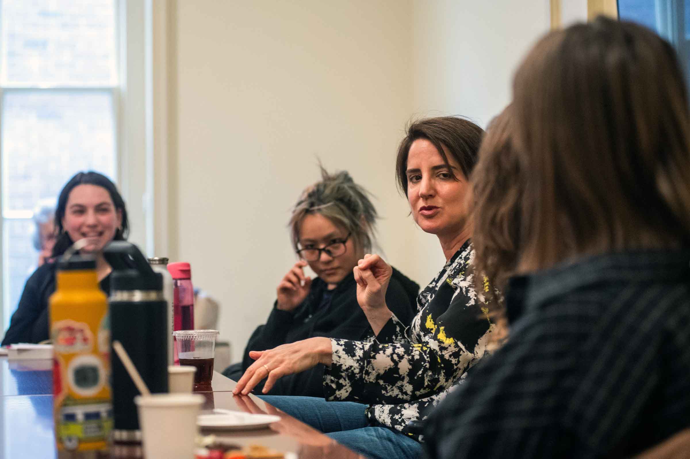 Five seated people at a table listening to one person, also at the table, speaking.