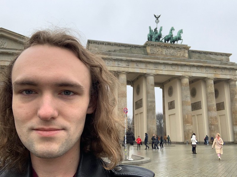 Person with long hair in front of an old marble building with classic columns.