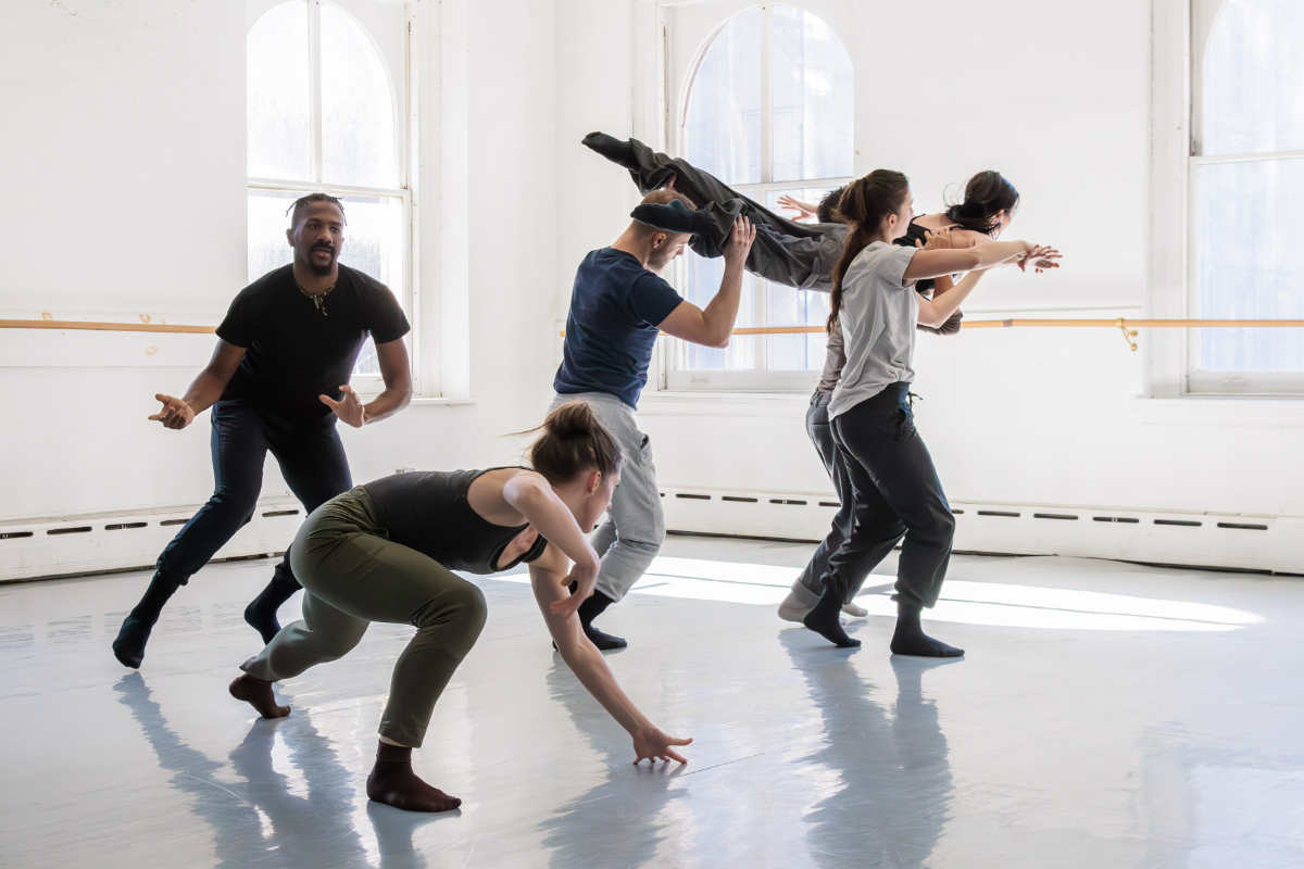 Six people practice dancing in a spacious, well-lit room.