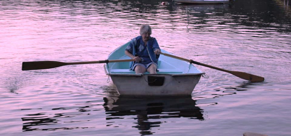 A photo of Jan Farrington ’46 rowing a boat in a lake at dusk.