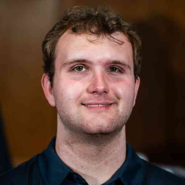 A person with short brown hair and a dark blue polo shirt smiles at the camera.