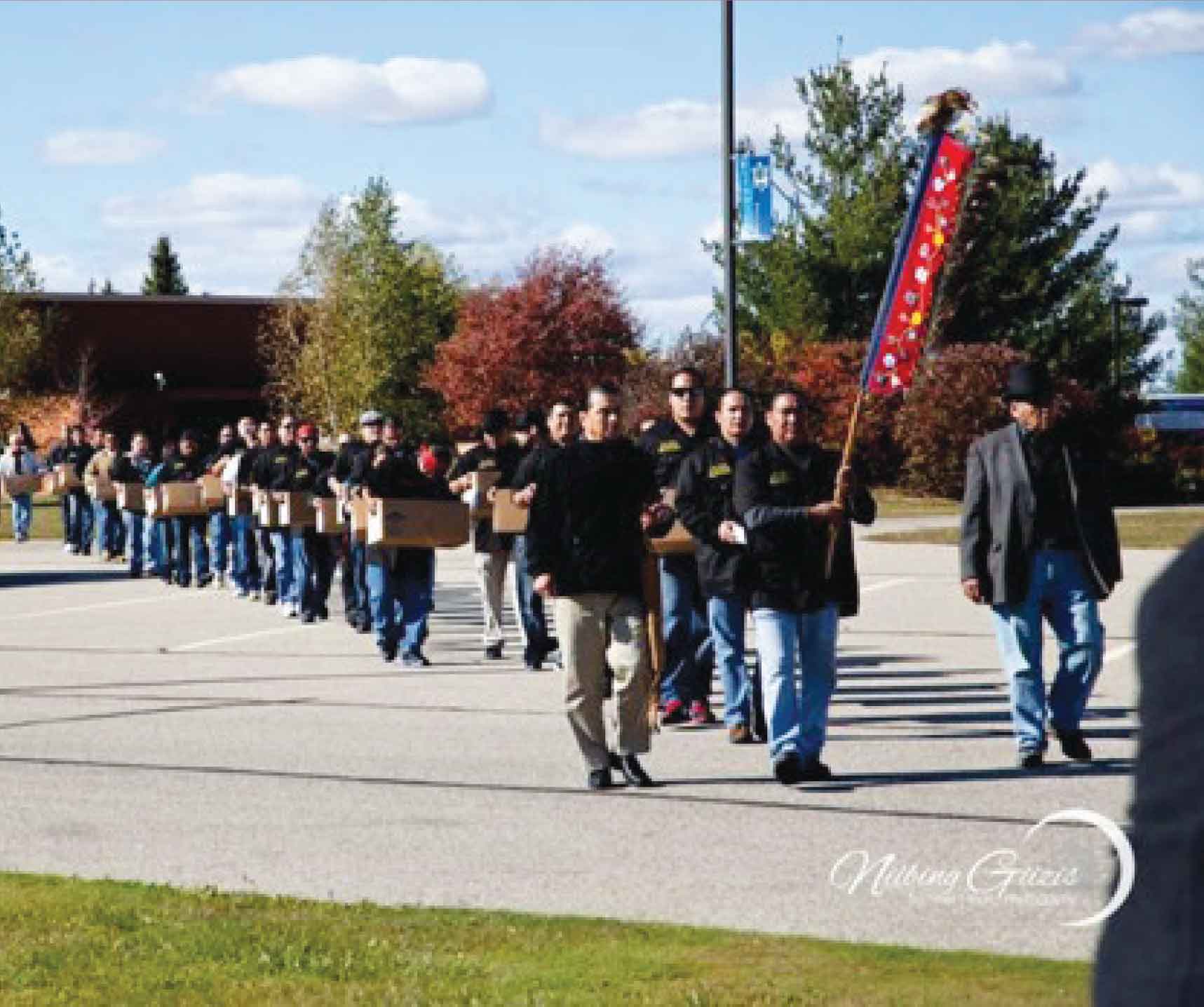 people walking in a parking lot behind a leader holding a flag.