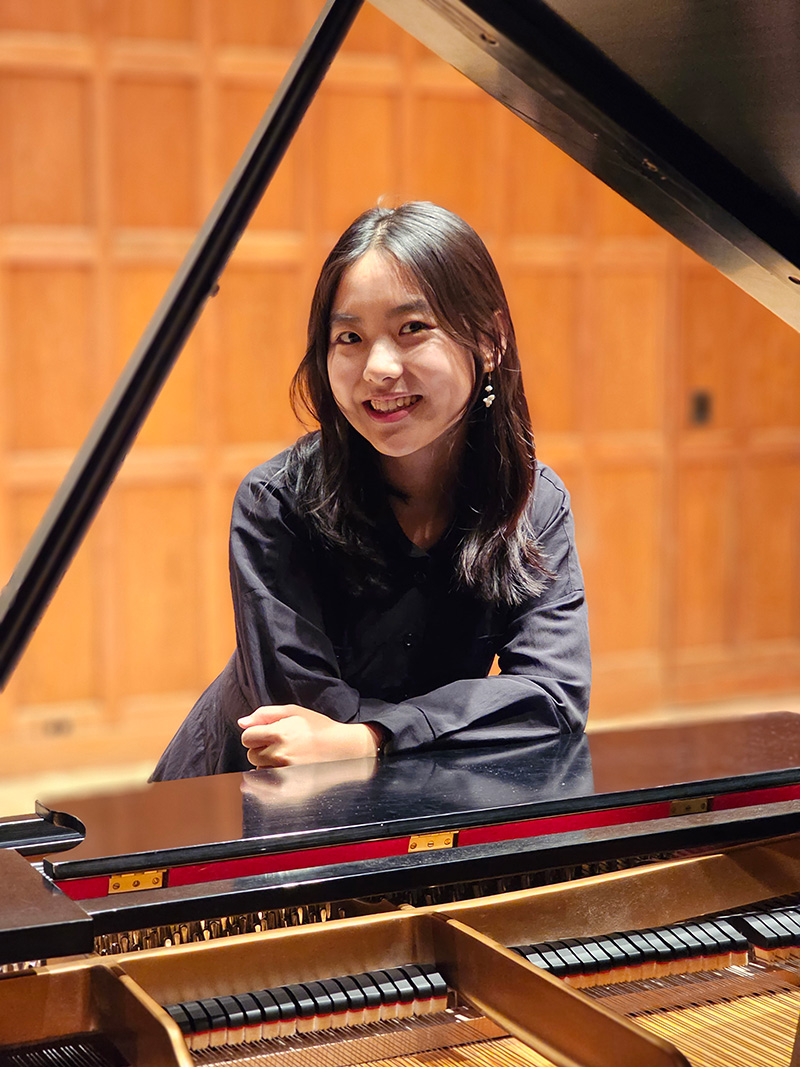 Looking through a piano with the top raised, a person leaning forward and smiling.