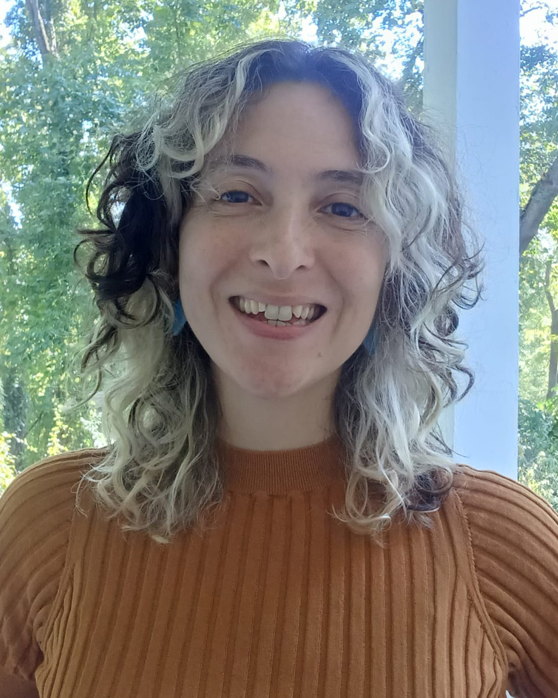 A person with medium long curly hair smiling brightly at the camera.