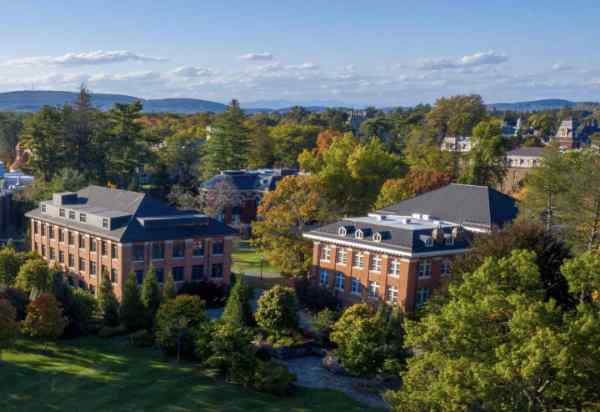 An aerial view of several classical brick buildings, trees, and green quads.