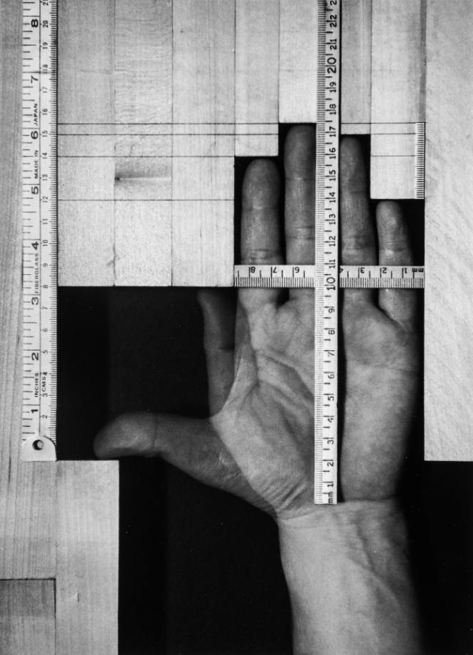A monochrome art photo of a hand, surrounded by geometrically arranged wood.