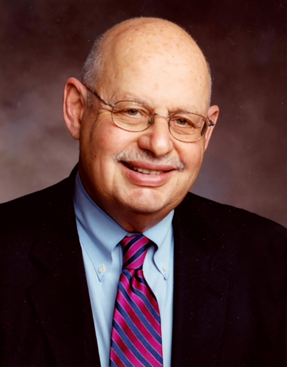 Dr. Daniel Aronzon wearing a black jacket, blue shirt and red tie.