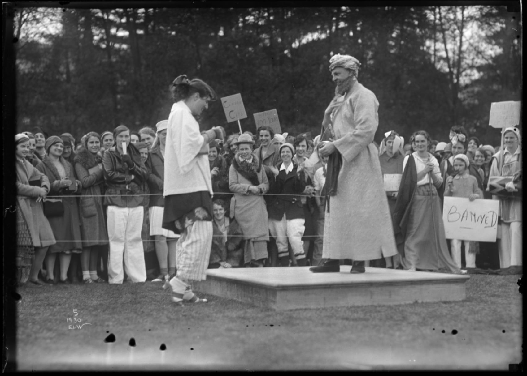 A black-and-white historical photo of people outside, performing in costumes that are intended to appear Middle Eastern.