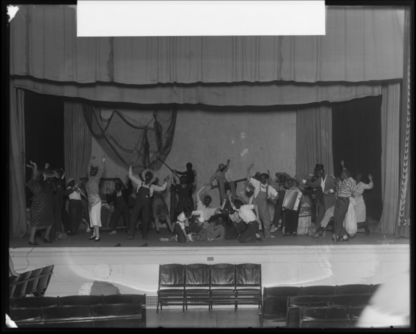 A black-and-white historical photo of Vassar students in racist blackface costumes, performing on stage in an indoor theater.