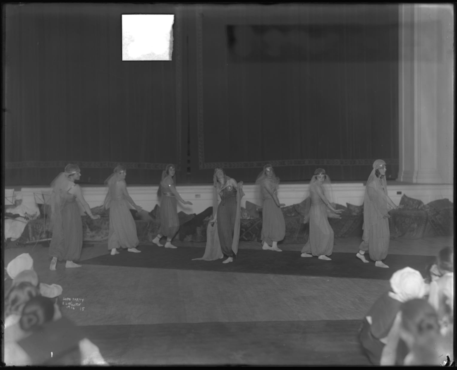 A black-and-white historical photo of people inside a theater, performing in costumes that are intended to appear Middle Eastern.