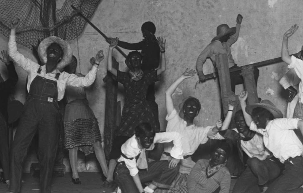 A black-and-white historical photo of Vassar students in racist blackface costumes, performing on stage in an indoor theater.