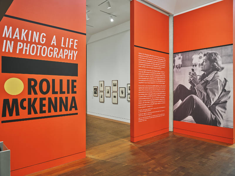 A photo of a large, spacious art gallery with a display on the walls that reads "Making a Life in Photography: Rollie McKenna" in large letters.