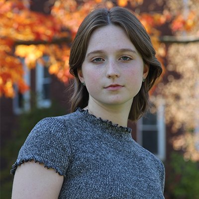 Portrait of Isabel Granger standing outside with autumn-colored leaves in the background.