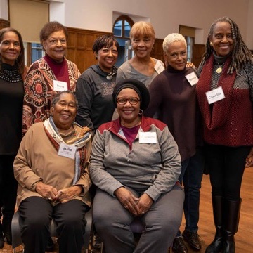 A group of people stand in a wood-paneled room, smiling at the camera.