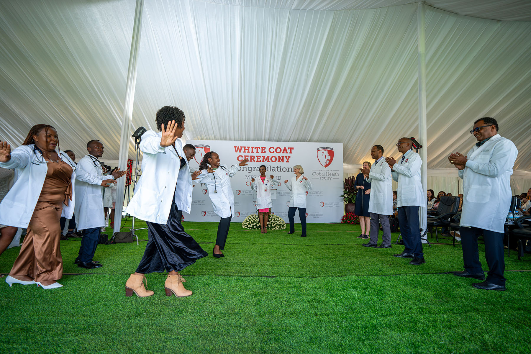 People dancing under a tent  with astroturf under foot clapping and wearing lab coats. 