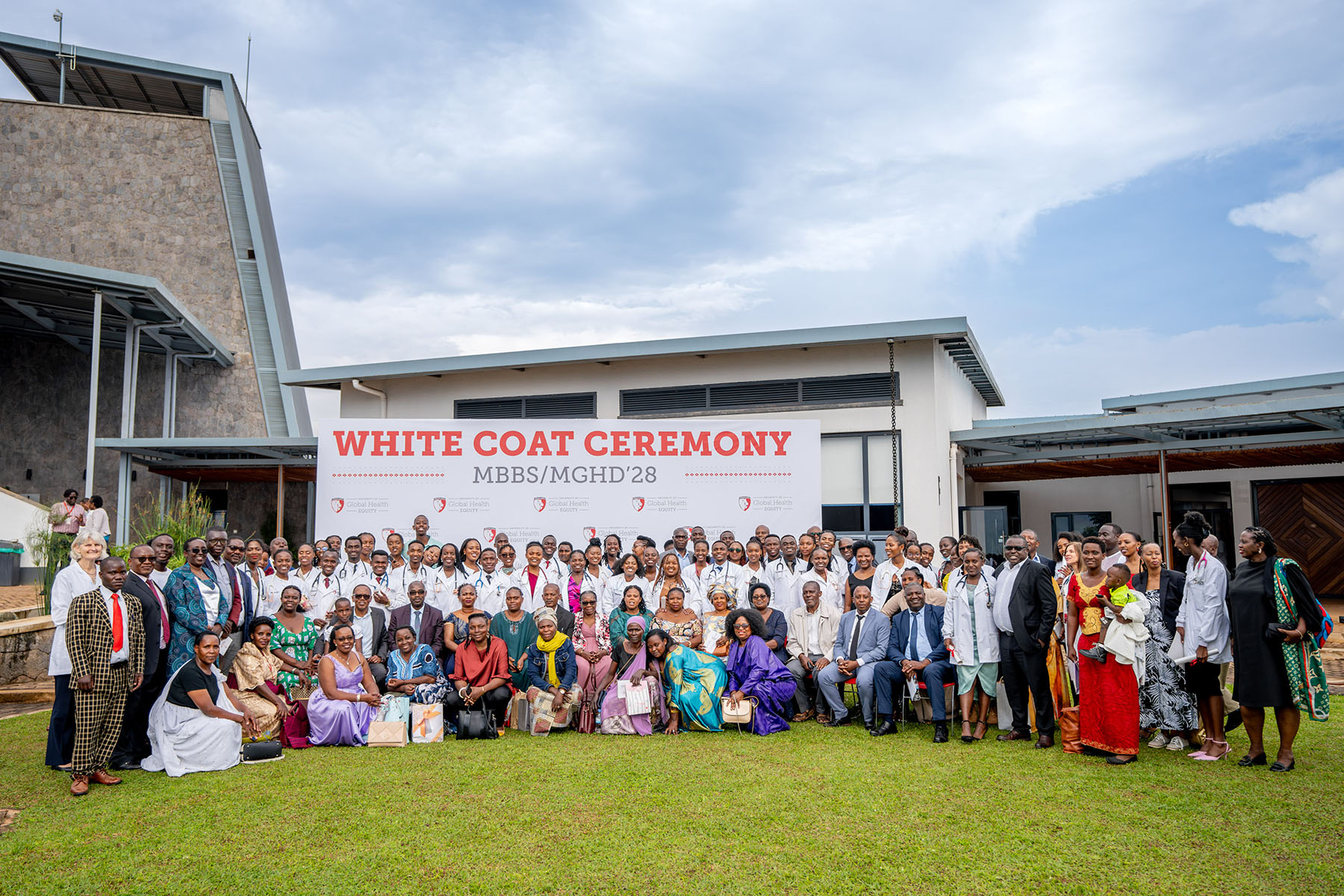 Rows of graduates posing outside next to a building in front of a tarp that reads, "White Coat Ceremony."