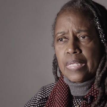 A photo of a person with long braided hair, speaking to the viewer.