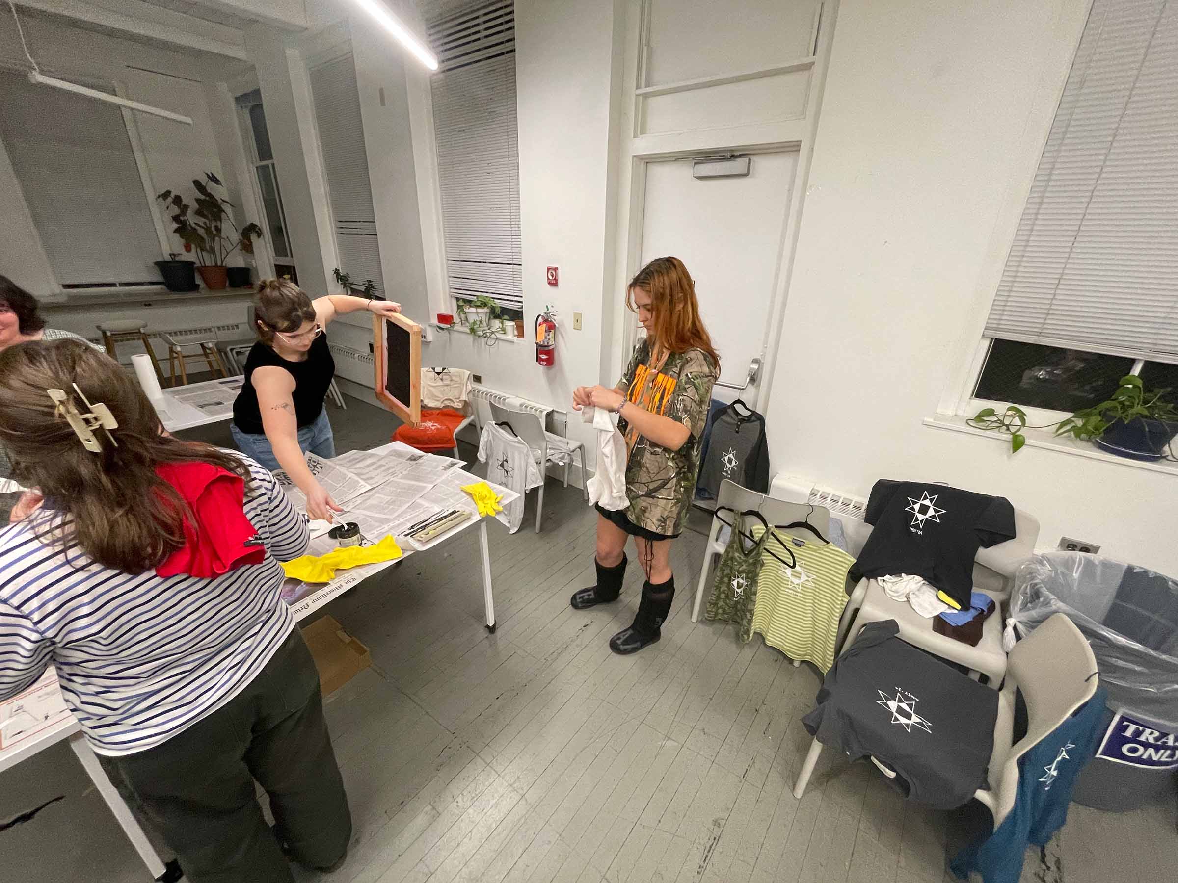 Students standing around a newspapered covered table making screen printed t-shirts.