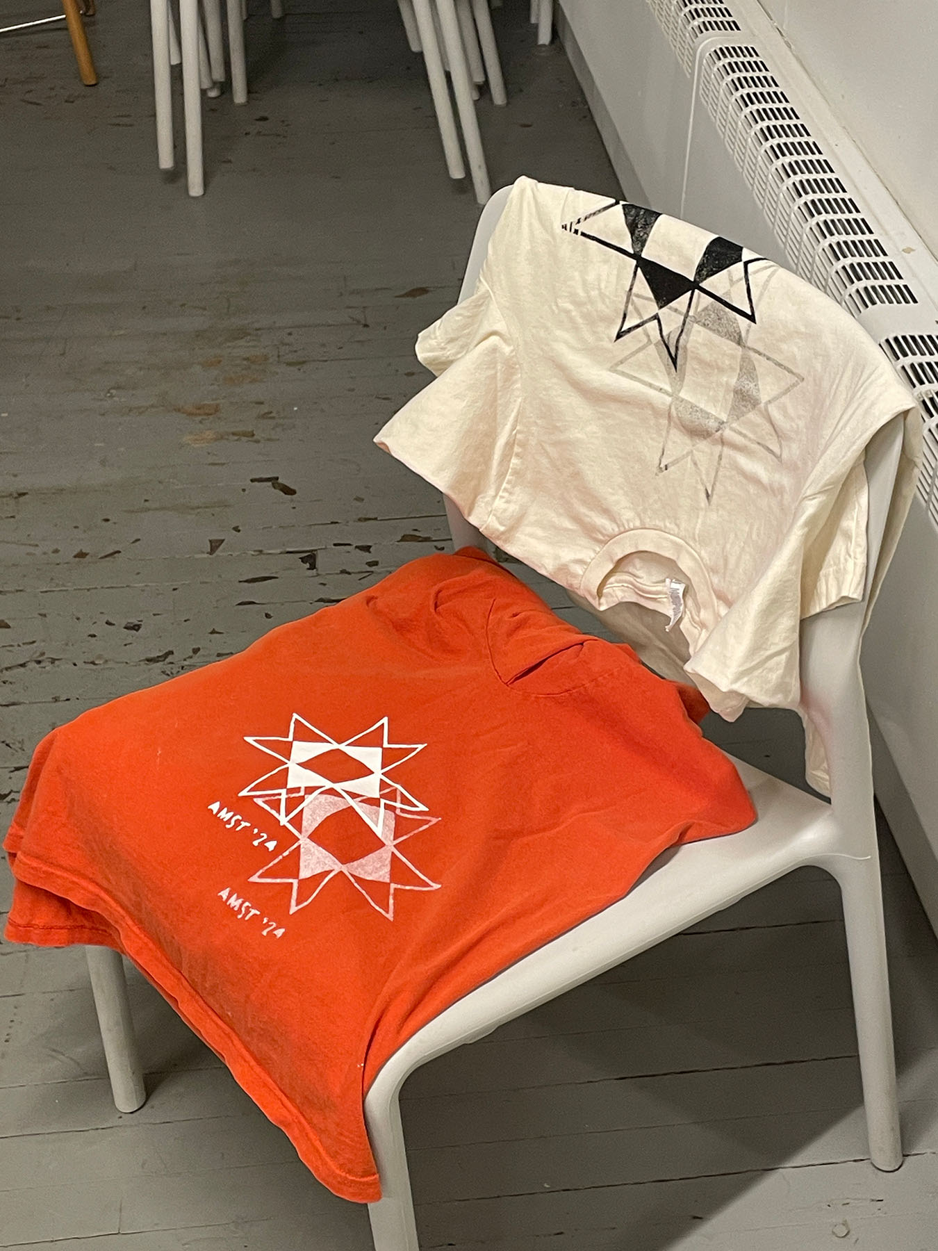 Orange and tan screen printed t-shirts hanging on a chair.