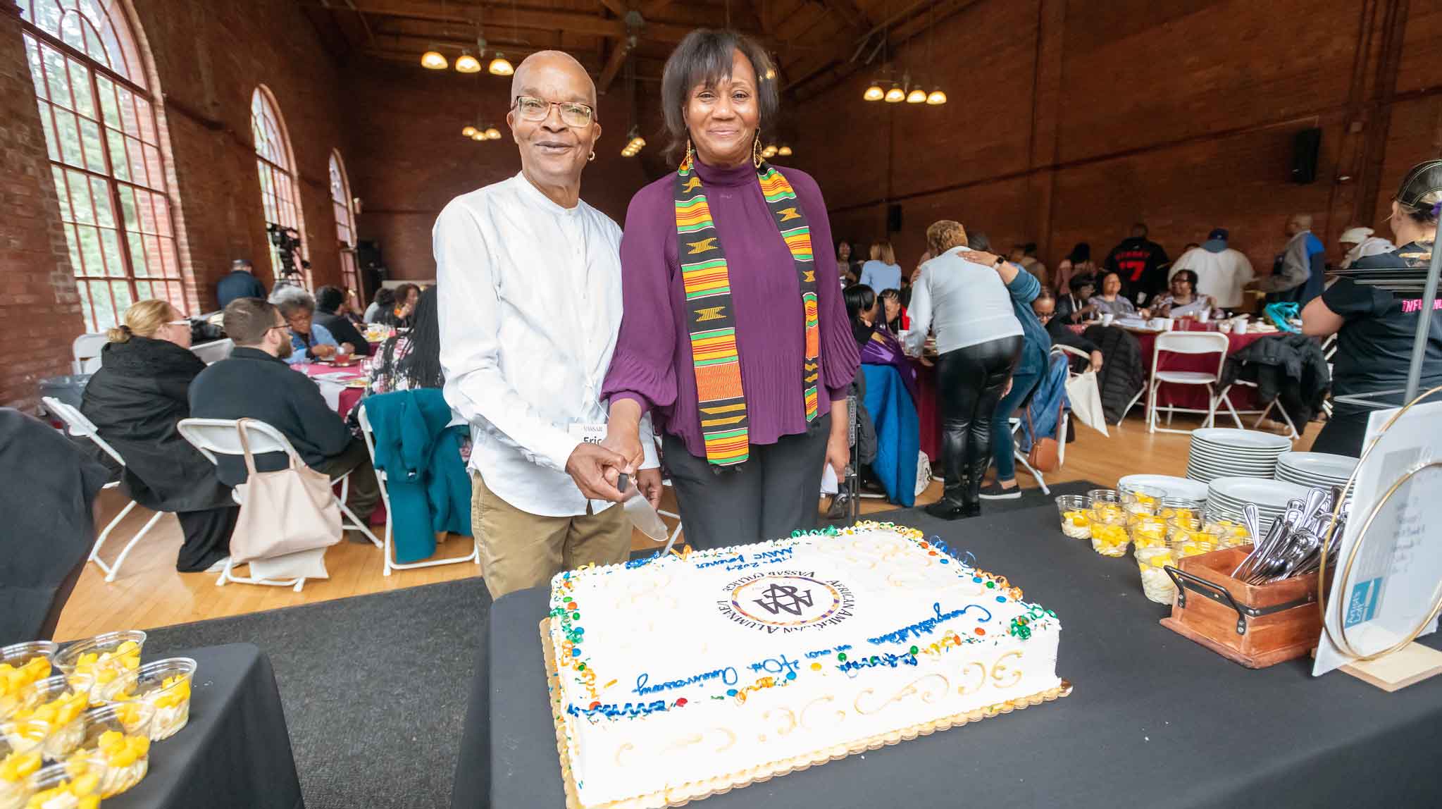 Two people smiling and holding hands while cutting a tabled cake together.