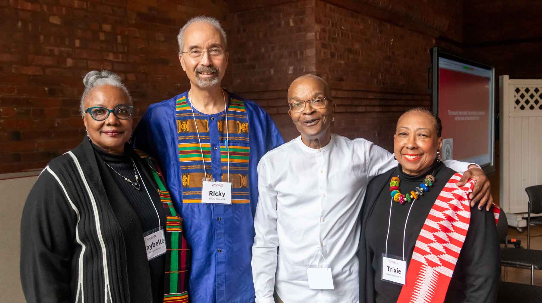 Four people standing arm in arm and smiling.