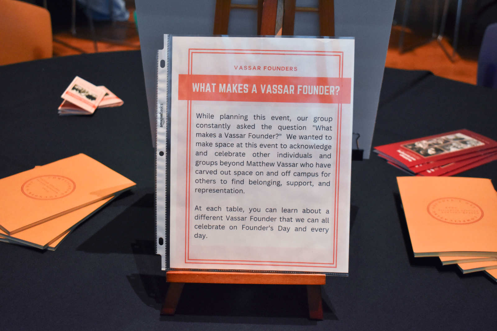 A poster placed on a table. The poster reads “Vassar Founders: What Makes a Vassar Founder? While Planning This Event, Our Group Constantly Asked the Question ‘What Makes a Vassar Founder?’.”