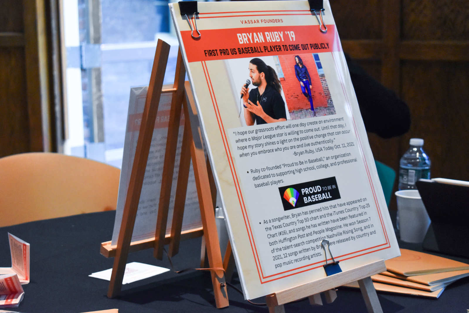 A poster placed on a table. The poster reads “Bryan Ruby '19: First Pro Us Baseball Player to Come Out Publicly.”