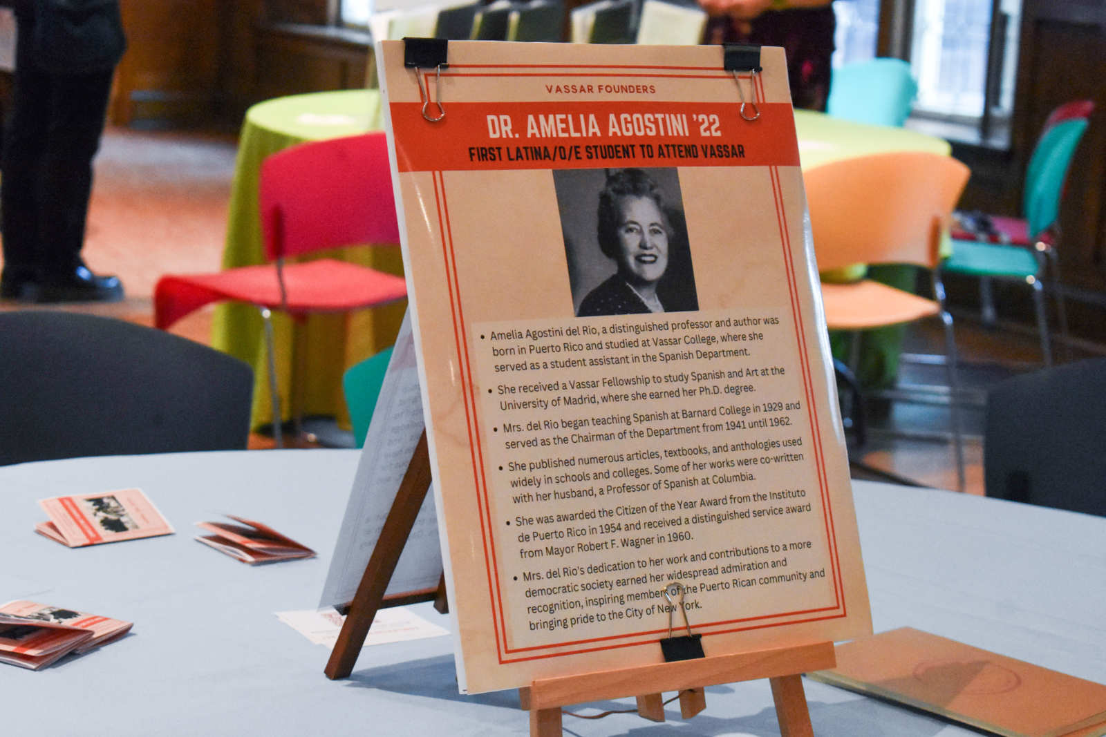 A poster placed on a table. The poster reads “Dr. Amelia Agostini ’22. First Latina/o/e Student to Attend Vassar.”