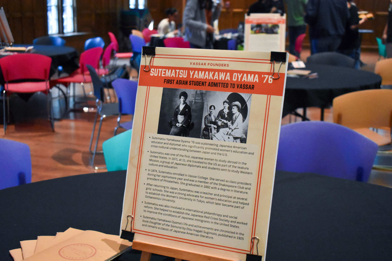 A poster placed on a table. The poster reads “Sutematsu Yamakawa Oyama '76: First Asian Student Admitted to Vassar.”