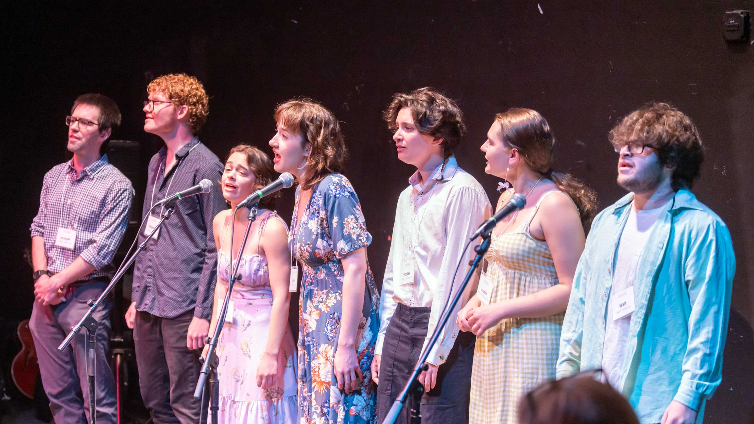 A group of people on staging standing behind microphones singing.