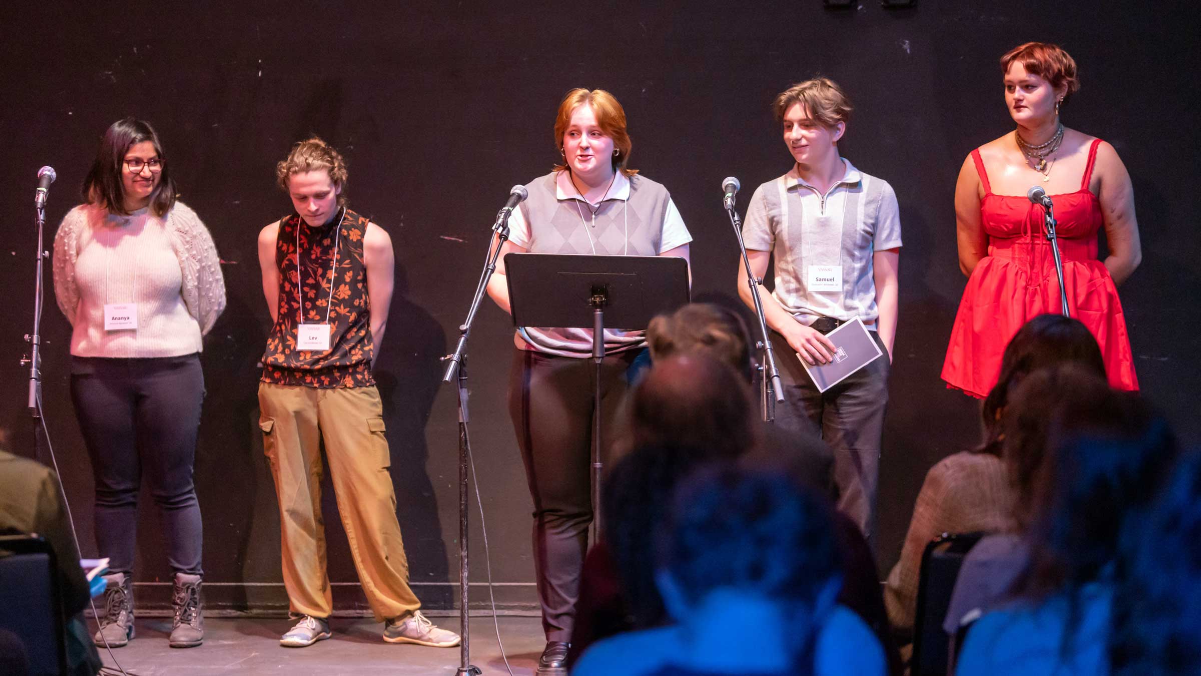 People standing on a stage behind a music stand and some microphones.